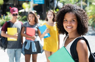 Student holding a book with her peers standing behind her. 