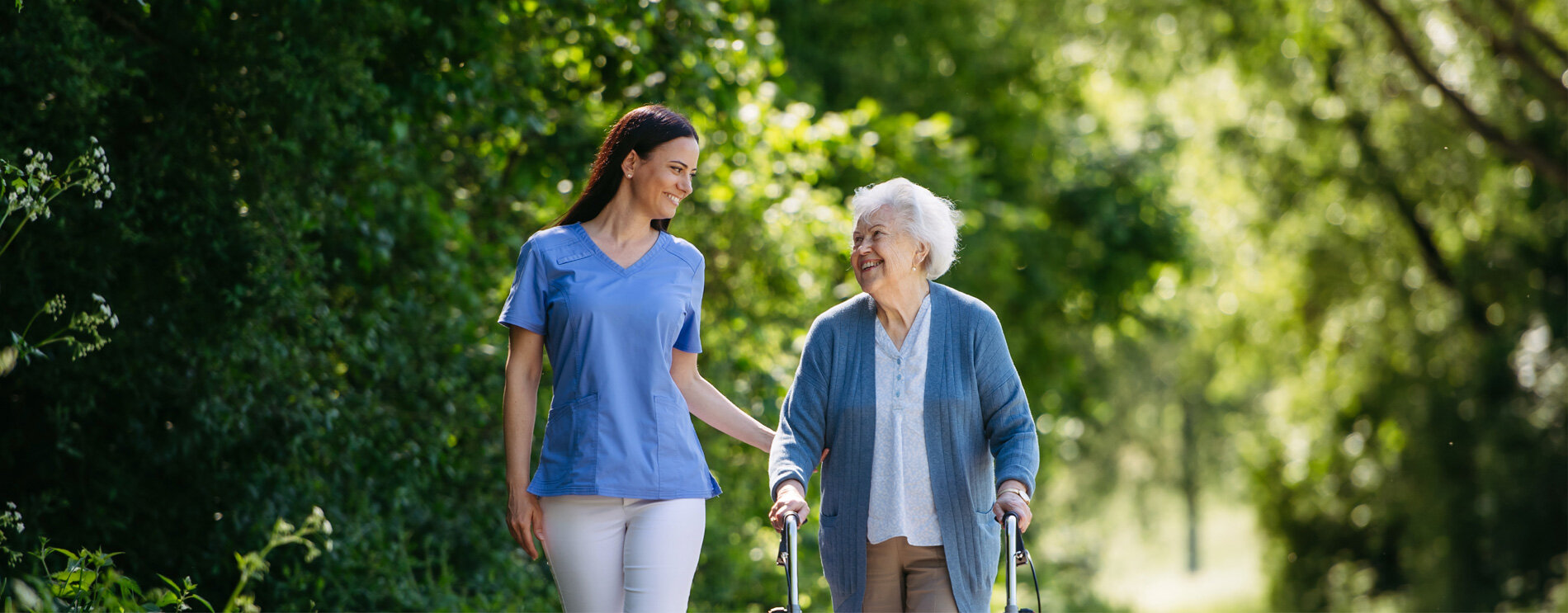 An elderly woman and an aide walking outside.