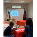 two ladies presenting in the front of a classroom and a little boy on his phone and a woman watching