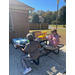 Two people are sitting at a picnic table that has Clorox wipes and face masks lined up; one of them is opening a box of face masks. 