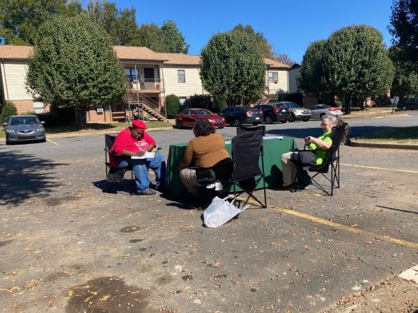 Two volunteer employees sit across from a resident that is filing out paperwork for her assessment.