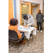 A gentlemen is leaned over the table and signing the sign-in sheet, while another man waits patiently behind him. 