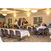 Several people are standing and sitting at the tables while they are talking and eating their food. 