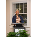 A woman with her hair tied up into a bun stands behind the podium and speaks into the microphone. 