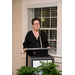 A woman wearing black-rimmed stands behind the podium and speaks into the microphone. 