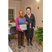 A woman with black-rimmed glasses stands with another woman in black-rimmed glasses who is holding open a certificate. 