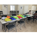 Two women sitting at a table doing paperwork at the table next to the table full of backpacks.