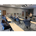 Wide angle view of the presentation speaker imparting knowledge to a group of men sitting at tables.