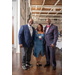  Two men and a woman, with one arm around each other, standing and smiling. 