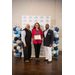  A woman smiles in a sport jacket holding a framed certificate with a man standing on either side of her. 