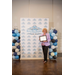  A smiling woman holding a framed certificate in front of a Rock Hill Housing Authority backdrop and balloons on either side.  